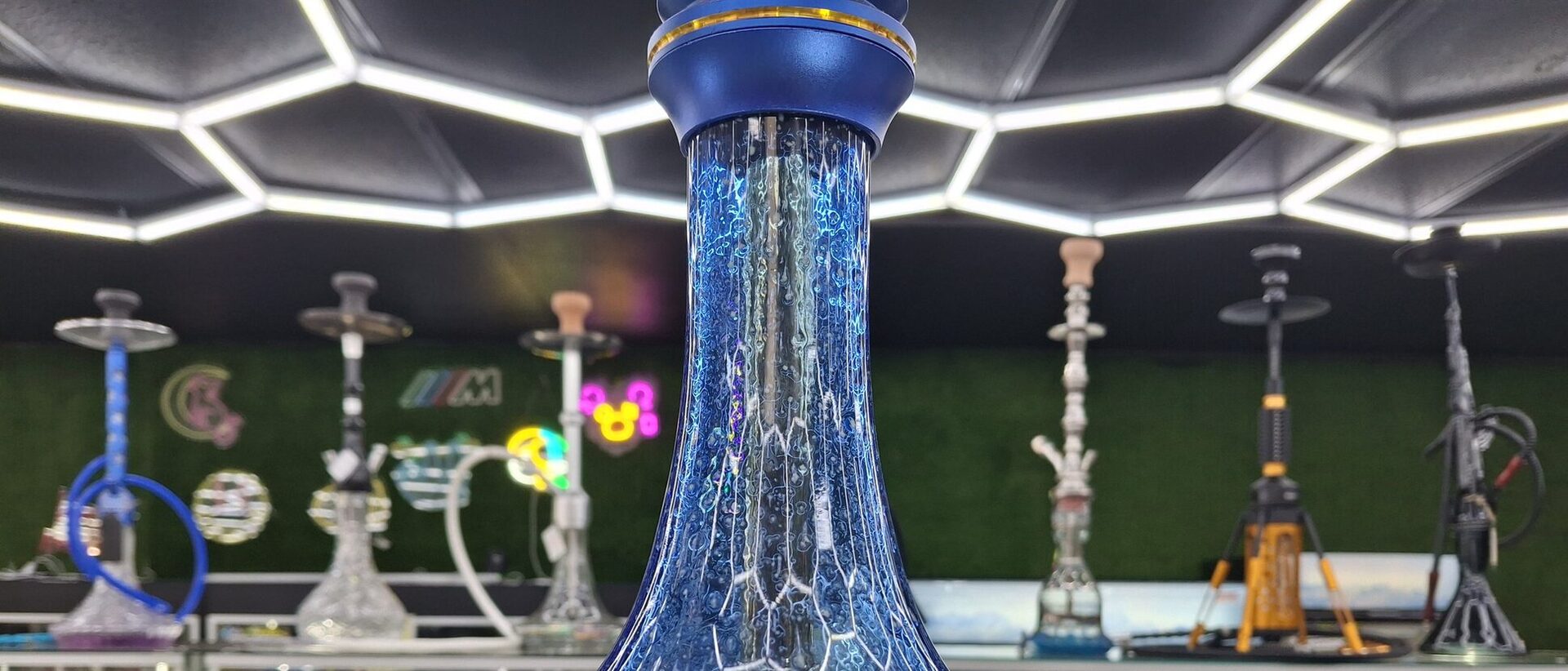 The Cloud Smoke Shop hookah room with a wall of hookahs under the hexagonal LED ceiling