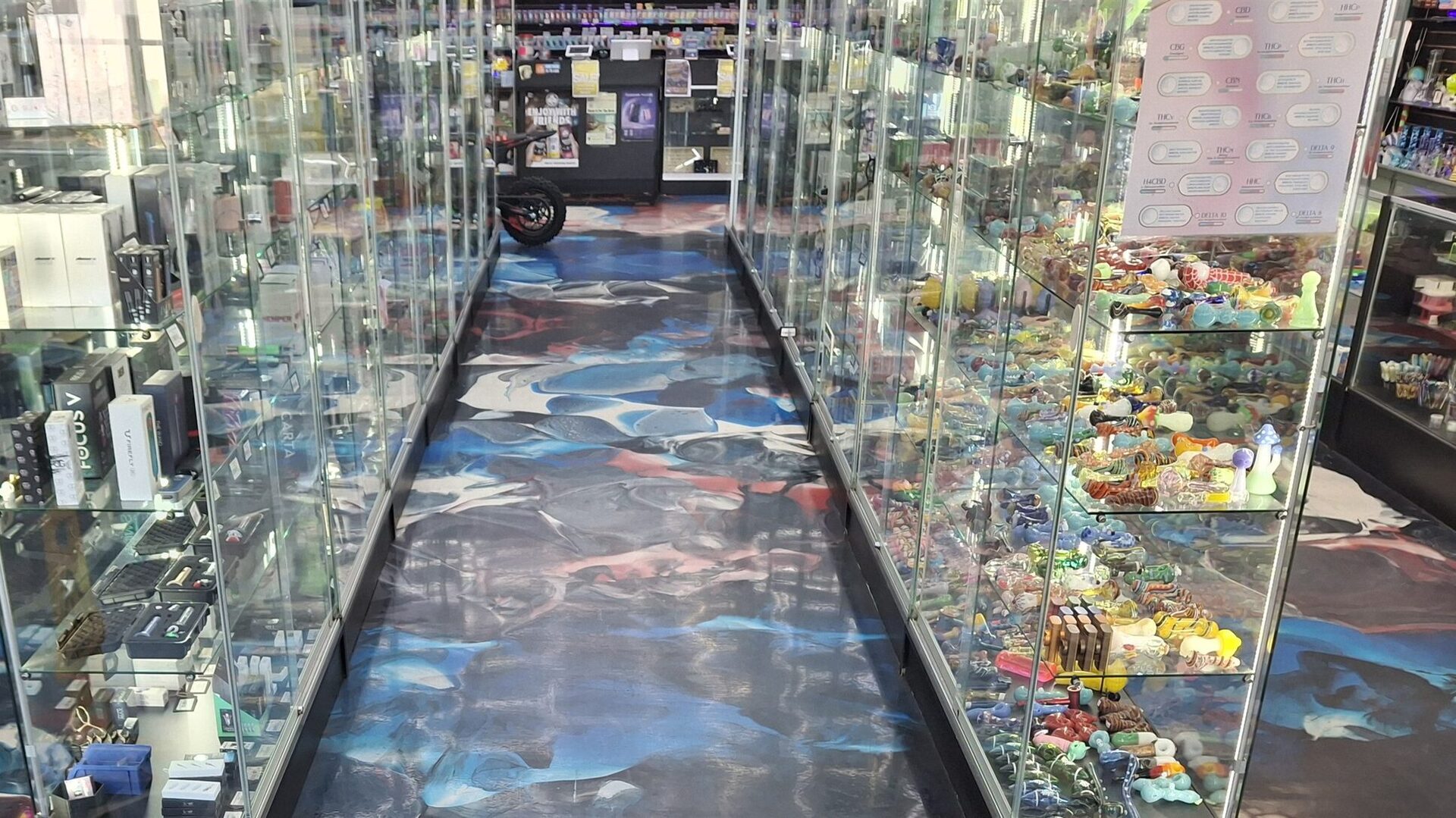 Lit glass display cases packed with colorful hand pipes along a Cloud Smoke Shop aisle